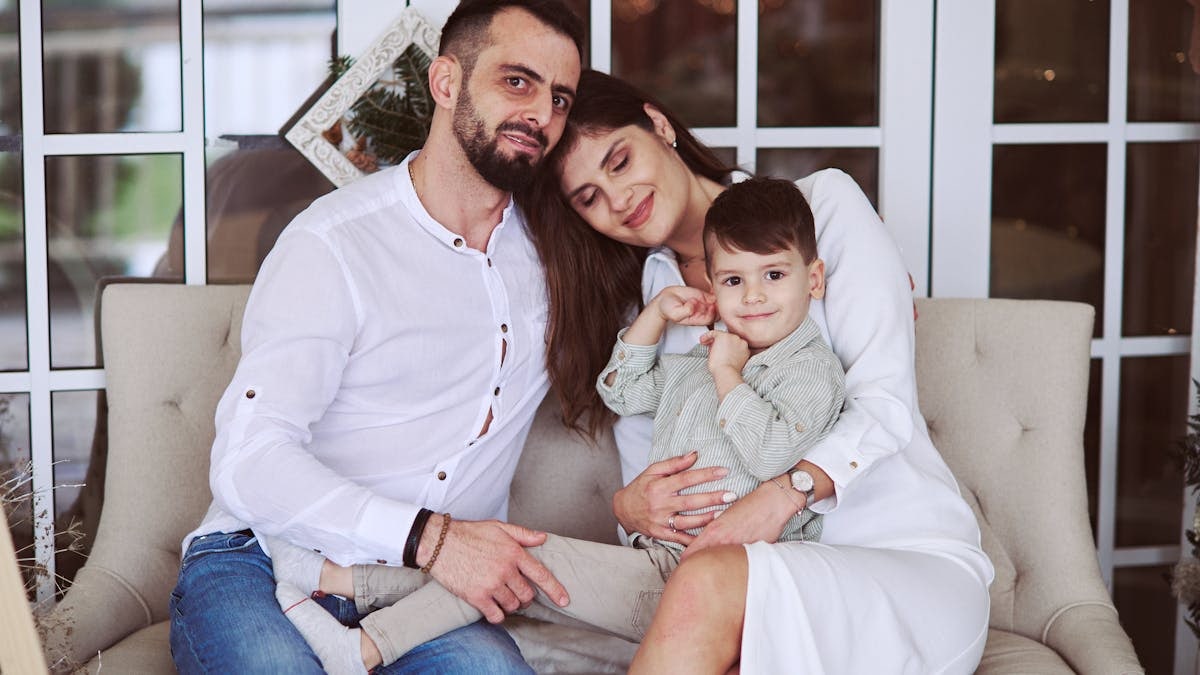 A family of three lovingly poses on a cozy sofa indoors, exuding warmth and togetherness.