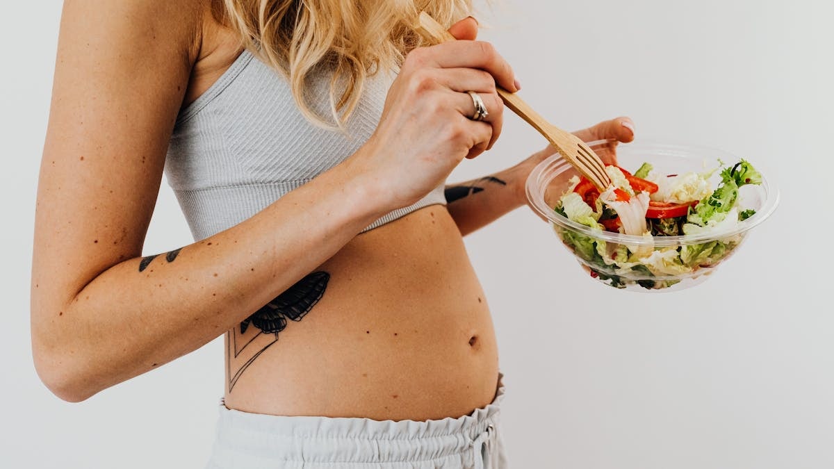 Close-up of a woman in a crop top enjoying a fresh salad indoors.
